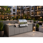 A stainless steel outdoor gas grill installed on a gray built-in kitchen island with a sink and countertop, set in a modern residential courtyard at dusk.